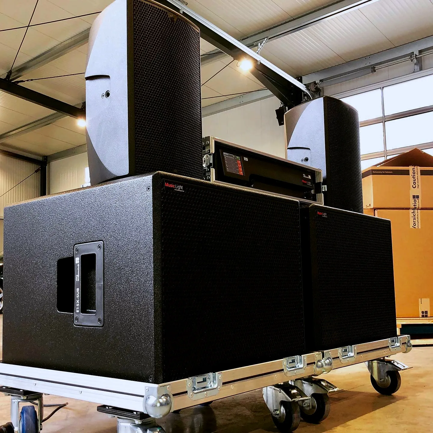 Zwei Subwoofer mit Topteilen und Endstufenrack, fahrbereit auf Rollbrettern im Lager